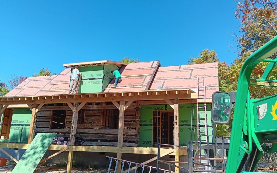 Workers installing roof panels on wooden house.