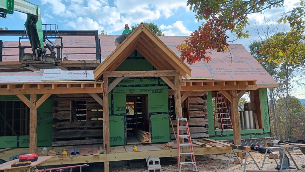 Log cabin construction with roof installation in progress.